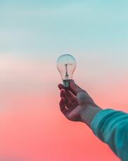 Someone holding a light bulb up against a dawn sky